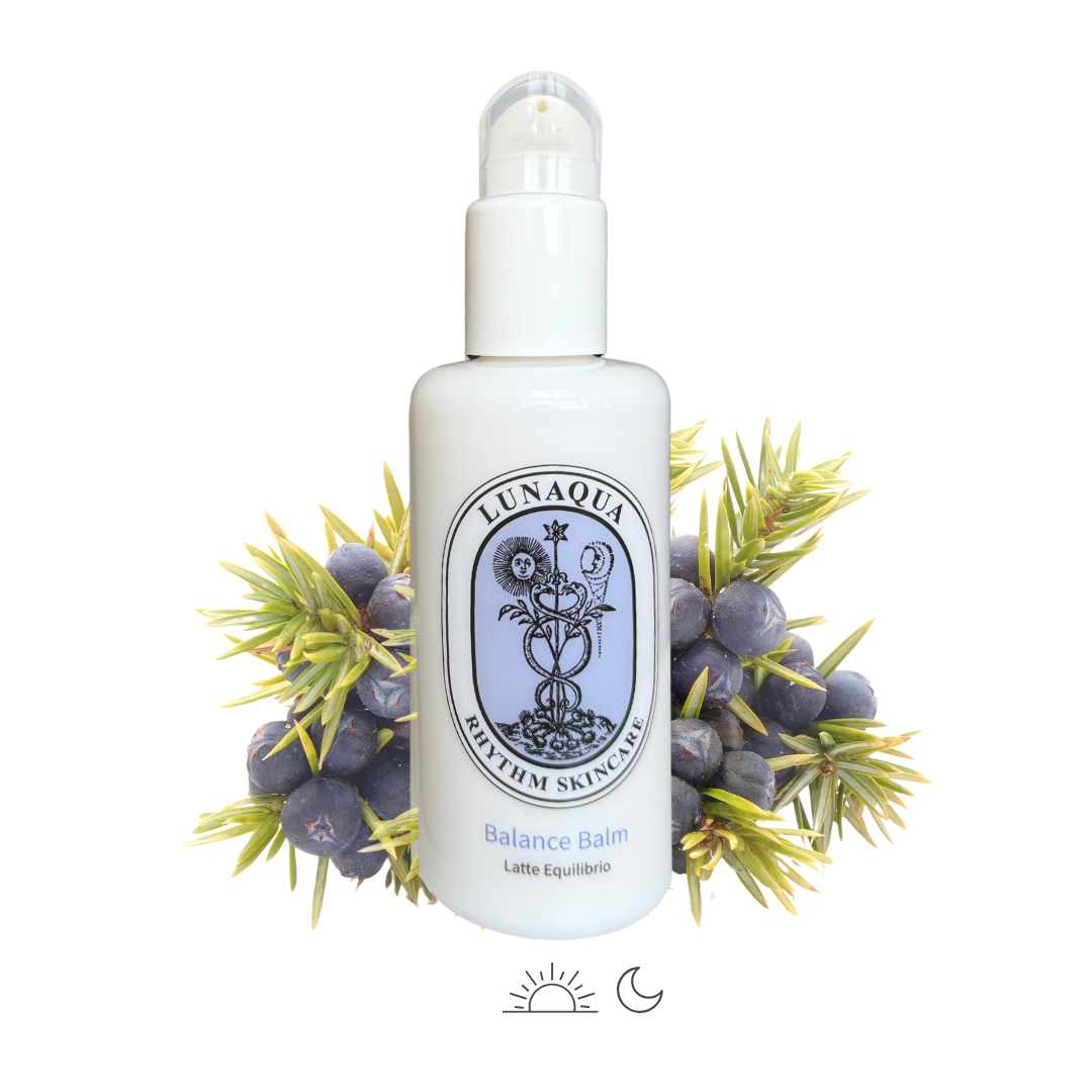 Bottle of Lunaqua Balance Balm surrounded by juniper berries and leaves on a white background